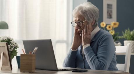 Elderly woman sitting at computer looking shocked